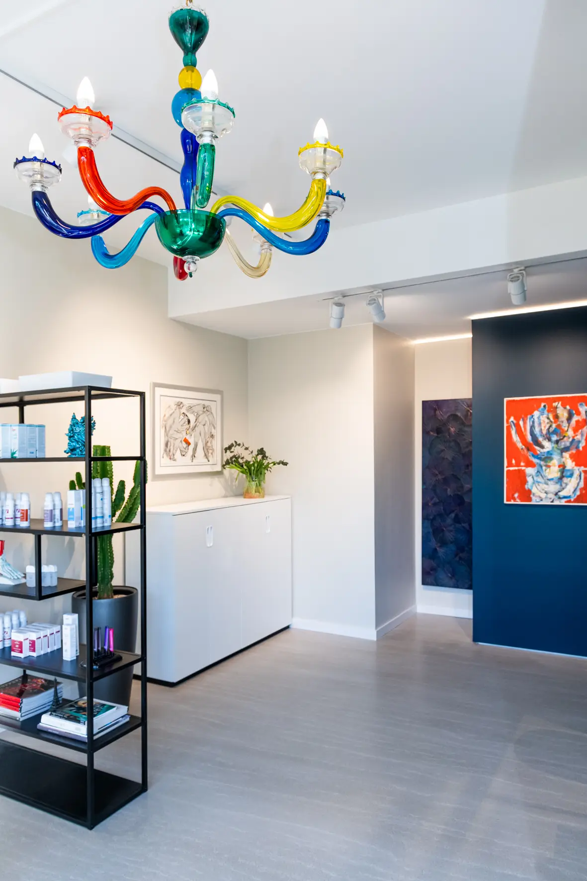 Eingangsbereich mit farbigem Glas-Kronleuchter, Regal mit Pflegeprodukten und Kunst an der Wand